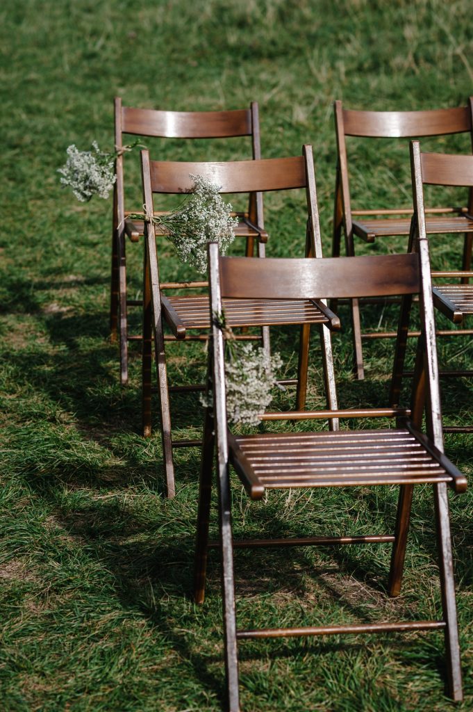 Wooden chairs for guests are decorated flowers and greens in the backyard banquet area. Wedding